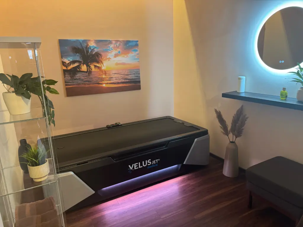 VELUSJET medical Massageliege in modernem Entspannungsraum mit Wandbild Sonnenuntergang am Strand